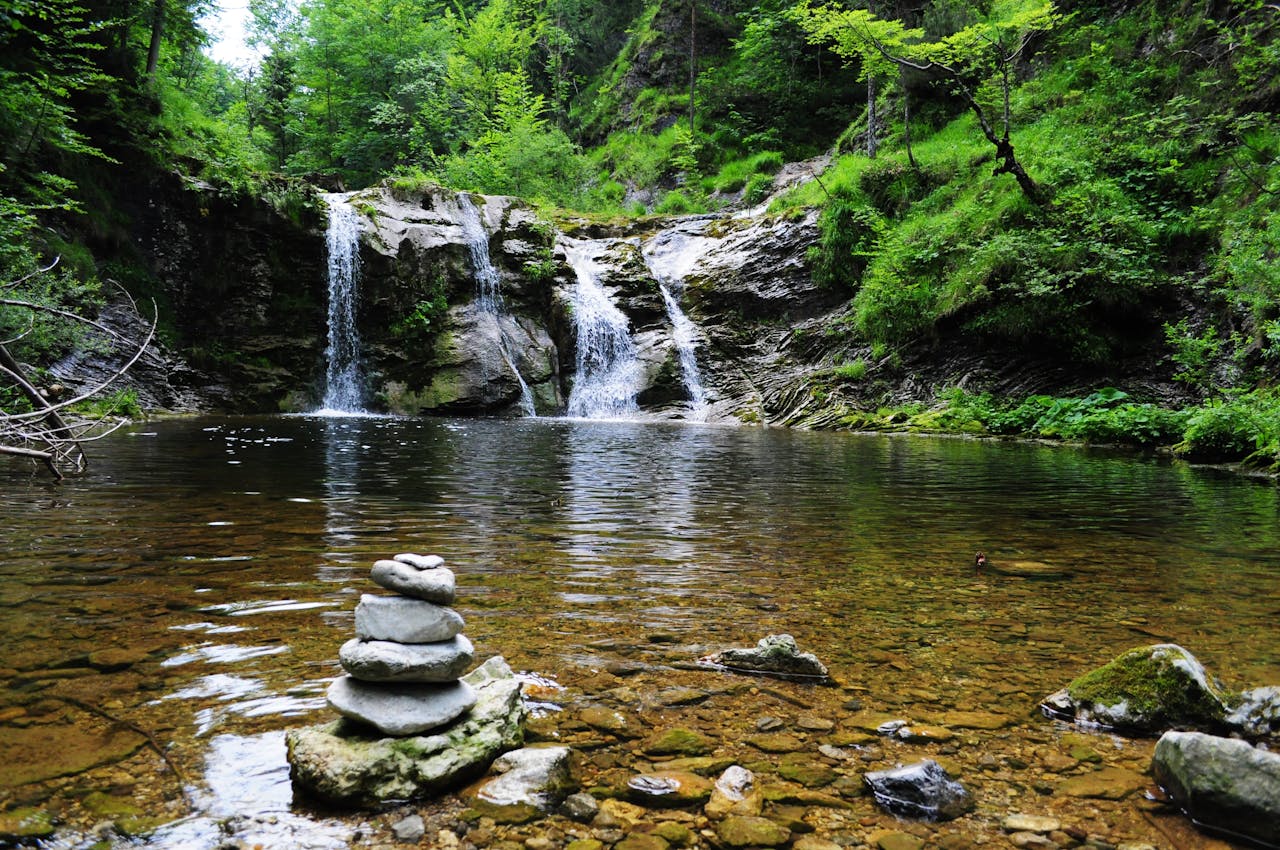Peaceful forest waterfall with serene stone cairn, ideal for nature and travel themes.